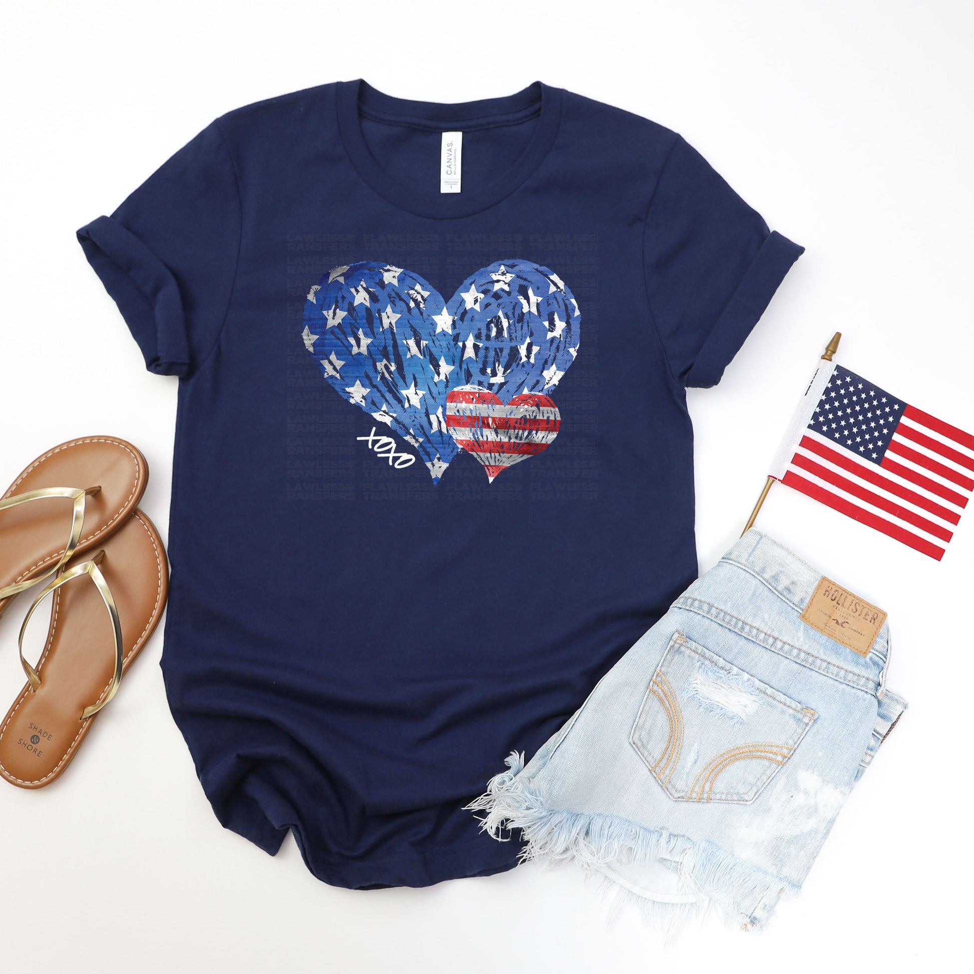 a casual outfit consisting of a navy blue t-shirt with a patriotic heart design, a pair of denim shorts with frayed edges, and a pair of sandals. The outfit is accompanied by an American flag and a pen, suggesting a patriotic theme or a special occasion.